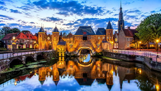 “Breedbeeldfoto van de iconische Koppelpoort in Amersfoort, Nederland, met historische stadsmuren en sfeervolle verlichting aan het water tijdens zonsondergang – professionele 8K landmarkfoto voor meubels herstofferen en meubelstoffering in Amersfoort.”