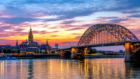 “Breedbeeldfoto van de iconische Waalbrug en historische skyline van Nijmegen, Nederland, met uitzicht over de rivier bij zonsondergang – professionele 8K landmarkfoto voor meubels herstofferen en meubelstoffering in Nijmegen.”